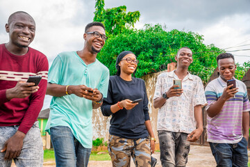 group of friends, walking together, laughing, having fun, using their mobile phones - obrazy, fototapety, plakaty