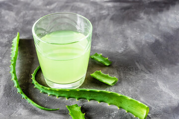 Aloe vera juice in a glass and fresh aloe leaves on a gray background in sunlight.