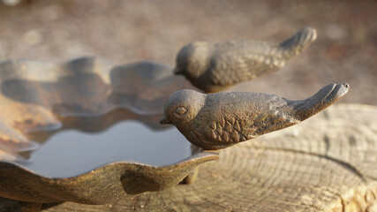 Two small decorative metal birds sitting on the edge of a clam shaped bird bath in the late autumn sun