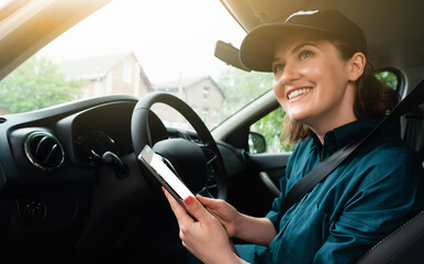 Woman courier sitting in a car and looking at a digital tablet