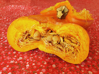 Broken pumpkin in half with scattered seeds on red material