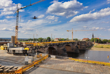 
construction site with wonderful typical yellow colored signs and a bridge, blue sky with white clouds and a plane flying around into the direction of the crane in Prague, Czechia