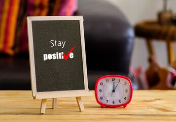 Image of motivational greeting Stay positive on chalk board. Besides a decorative green plant in vase. Selective focus on notice board. Others in gradient blur.