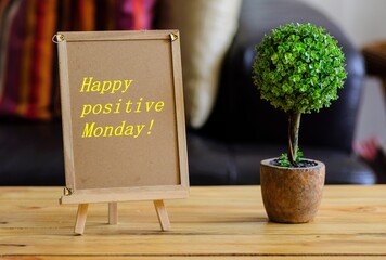 Image of motivational greeting happy positive Monday on brown mini notice board. Besides a decorative green plant in vase. Selective focus on notice board. Others in gradient blur