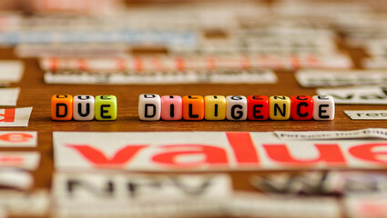 Colorful letter beads DUE DILIGENCE with common business-related title from newspaper cuts. Selective focus on beads only.