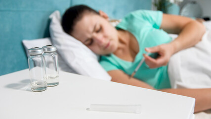 Obraz premium Blurred image of sick woman with diabetes lying in bed and making insulin injection with syringe