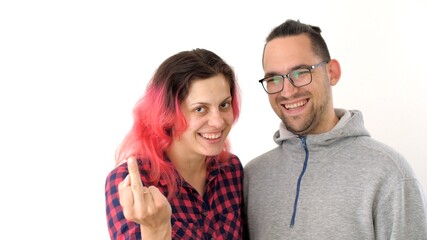 Man and a woman hug, laugh and play the fool. Modern hipster family. Wife with pink hair and husband with long hair ponytail show indecent gestures to the camera. 