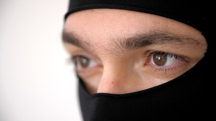 Close-up portrait of a man in a black balaclava. Brown eyes close up. Thief or burglar. Riots,...