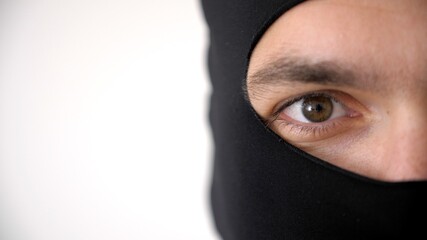Close-up portrait of a man in a black balaclava. Brown eyes close up. Thief or burglar looks at the...