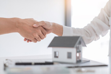 Estate agent in suit sitting in an office desk shaking hands with customer after contract signature...