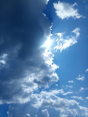 Photo of a blue summer sky with clouds from which the sun peeps