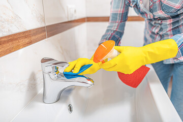 Cleaning in the bathroom. A woman wipes the sink and washbasin faucet.