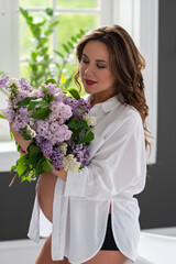 Beautiful pregnant woman in a white shirt in the bathroom near the window with a bouquet of lilac flowers. Soft selective focus.