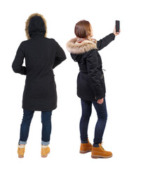 Back view of two young woman photographed on a mobile phone in winter jacket.