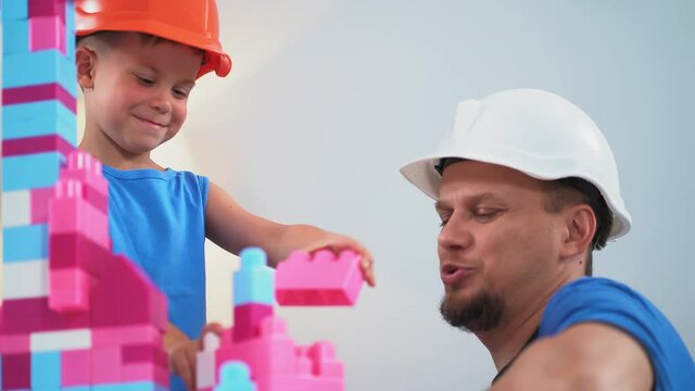 Father with his son wearing construction helmets playing brick constructor helping him showing how to build castles correctly. June 2019.Kiev, Ukraine. Prores 422. 