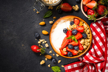 Greek yogurt granola with fresh berries on black stone table.