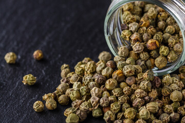 green peppercorns on dark slate stone background