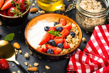 Greek yogurt granola with fresh berries on black stone table.