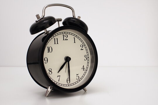 Black vintage alarm clock on table. White background. Wake up concept. An image of a retro clock showing 07:30 pm/am.  