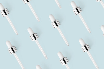 Glass pipettes pattern on light blue minimalist pastel background. Concept skin care product, top view. Repetition dropper beauty wallpaper