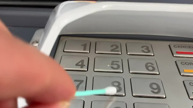 Man typing his secret code on an ATM with a cotton swab for avoiding contamination with germs and virus like COVID-19 coronavirus.