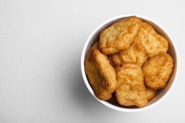 Bucket with delicious chicken nuggets on light background, top view. Space for text