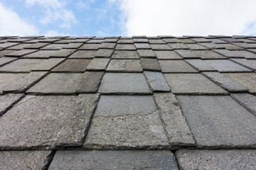 Old roof slate tiles roof with blue sky and clouds.