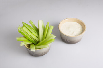 close up isolated top corner view shot of a bowl of crunchy juicy green celery sticks next to a white cup of blue cheese dipping sauce on a white background