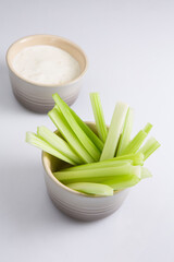 vertical close up isolated top view shot of a bowl of crunchy juicy green celery sticks next to a...