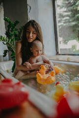 Mother bathes in bathtub and hugs her baby.