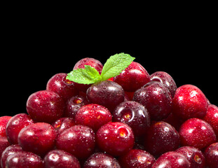 Ripe cherries on a black background, isolate. Red berry, food for a vegetarian. Ripe cherry with green leaves.
