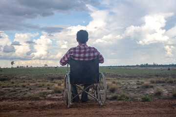 Young disabled man with field background.He is sitting on wheelchair.He is looking into sky.despair,lonely,hope.Photo concept depression and Patient.