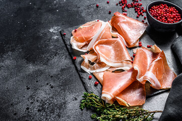 Spanish jamon Serrano with thyme, cured ham. Black background. Top view. Copy space