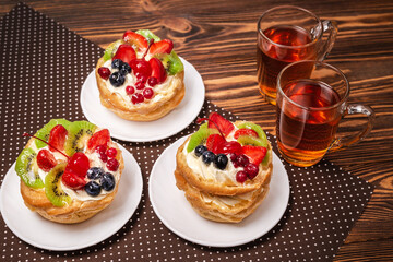 Home made cake with cream and fruit and hot tea on wooden table.