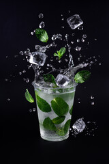 Fototapeta na wymiar Ice cubes and mint leaves splashing into glass of lemonade. Black background