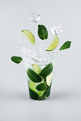 Ice cubes, slices of lime and mint leaves splashing into glass of lemonade. Light grey background