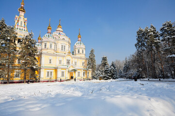 Brightly painted Ascension Cathedral in Almaty's Panfilov Park on a snowy winter's day under a clear blue sky.