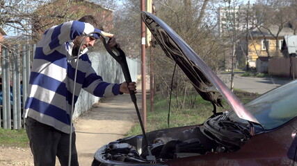 A man washes away dirt from a car engine with a high-pressure water jet. Special detergent for car wash. Washes a car in front of the house.