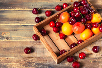Ripe seasonal summer fruits in rustic wooden case. Juicy red cherry and orange apricot. Delicious light sweet dessert.Wooden background, copy space for your text. Tonned. Flat lay top view