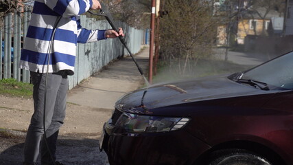 A man washes dirt off a car with a high-pressure water jet. Special detergent for car wash. Washes a car in front of the house.