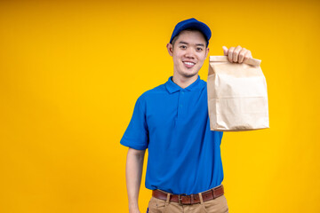 Asian delivery man holding fast food bag over yellow isolate background. Work from home and delivery concept.