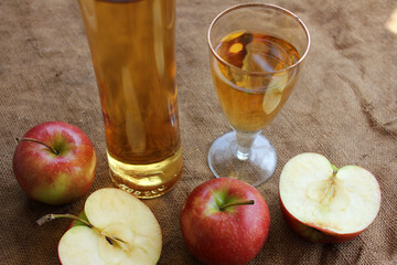 Homemade apple cider in a bottle and in a glass, and fresh apples on a burlap background, top view, copy space.
