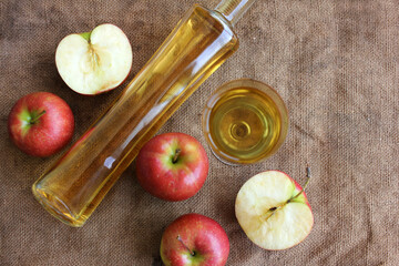 Homemade apple cider in a bottle and in a glass, and fresh apples on a burlap background, top view, copy space.

