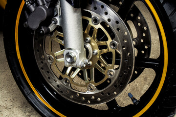 Front wheel with brake discs of a sports motorcycle close-up on concrete. Rubber with black alloy disc, brake system of a road bike in a garage