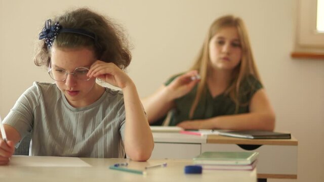 Schoolgirl from the last desk throws a piece of paper at her friend. Misses. Normal school routine after quarantine life, back to school. Classmates teens in classroom