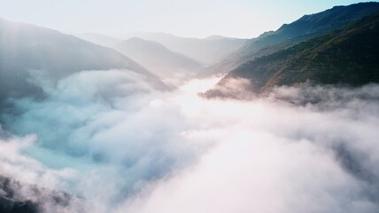 Aerial/Drone View of a foggy Himalayan valley and green fields surrounded by lush green hills during a beautiful morning at a rural location in Uttarakhand, India.