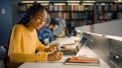 University Library: Gifted Black Girl uses Laptop, Writes Notes for the Paper, Essay, Study for Class Assignment. Diverse Multi-Ethnic Group of Students Learning, Studying for Exams, Talk in College - obrazy, fototapety, plakaty