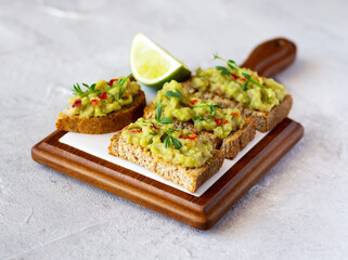 Guacamole toasts on a wooden board with slice of lime. Healthy snack
