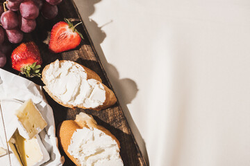 top view of of french breakfast with baguette, Camembert, strawberries and grape on wooden cutting board on white tablecloth