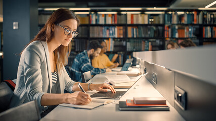 University Library: Talented Caucasian Girl Sitting at the Desk, Uses Laptop, Writes Notes for the Paper, Essay, Study for Class Assignment. Diverse Group of Students Learning, Studying for Exams.